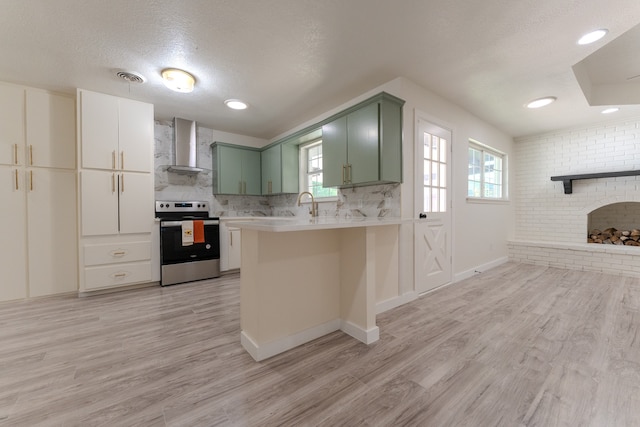 kitchen with kitchen peninsula, green cabinetry, wall chimney exhaust hood, stainless steel range with electric cooktop, and light wood-type flooring