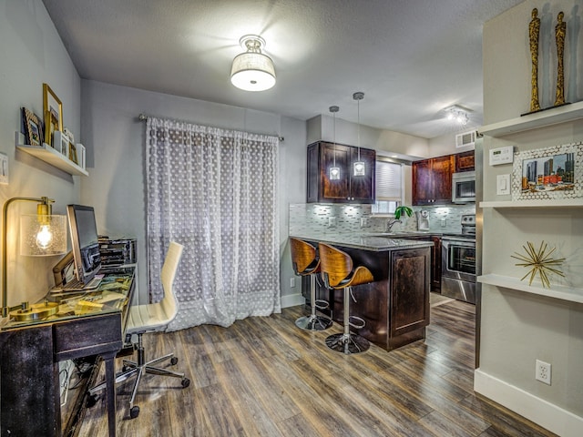 kitchen featuring appliances with stainless steel finishes, kitchen peninsula, a kitchen bar, and dark hardwood / wood-style floors