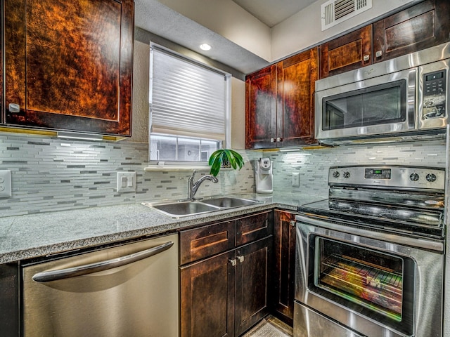 kitchen featuring appliances with stainless steel finishes, light stone counters, decorative backsplash, and sink