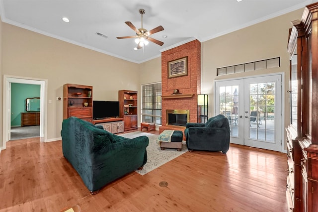 living room featuring ornamental molding, french doors, a brick fireplace, and light wood-type flooring