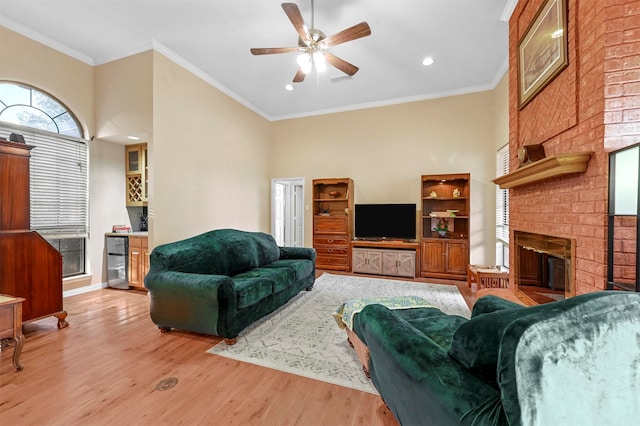 living room featuring a brick fireplace, ceiling fan, light wood-type flooring, and crown molding