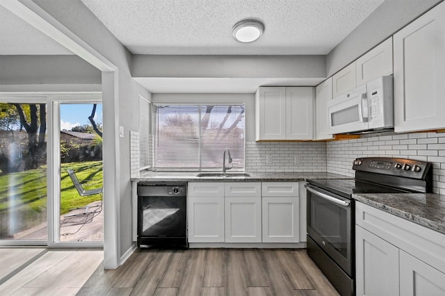 kitchen featuring sink, dishwasher, white cabinetry, dark stone countertops, and electric range