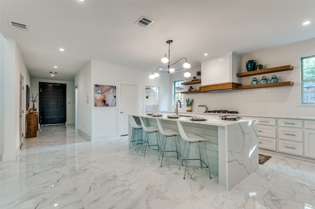 kitchen with a kitchen island with sink, white cabinets, decorative light fixtures, and a kitchen breakfast bar