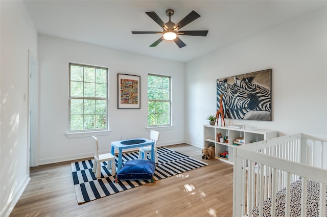 bedroom with ceiling fan, light wood-type flooring, and a crib