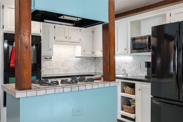 kitchen featuring tile countertops, white cabinetry, black refrigerator, ventilation hood, and decorative backsplash