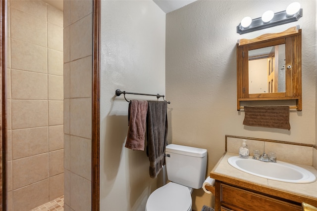 bathroom featuring toilet, a tile shower, and vanity