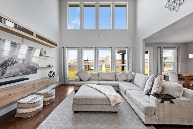 living room with a wealth of natural light, a towering ceiling, and dark wood-type flooring