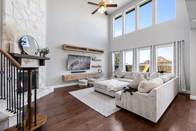 living room featuring a fireplace, a towering ceiling, dark hardwood / wood-style floors, and ceiling fan