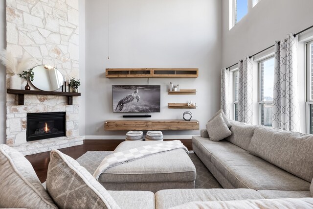 living room with hardwood / wood-style floors, a stone fireplace, and a high ceiling