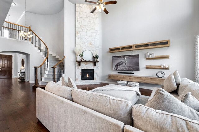 living room with a stone fireplace, ceiling fan with notable chandelier, dark hardwood / wood-style floors, and a high ceiling