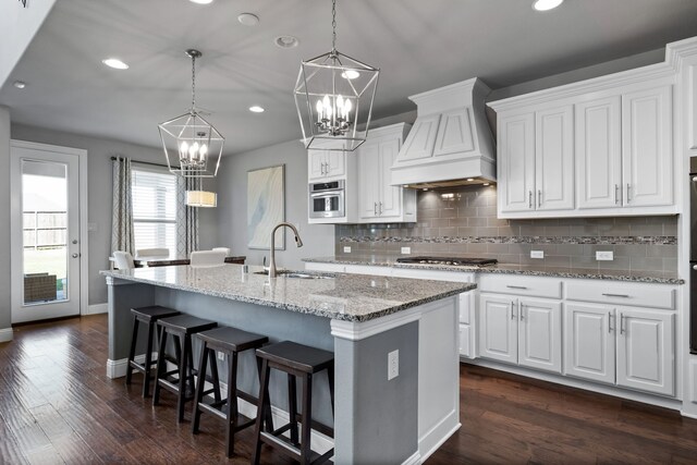 kitchen featuring white cabinets, stainless steel appliances, a kitchen island with sink, and custom exhaust hood