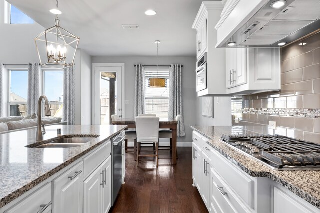 kitchen featuring custom exhaust hood, stainless steel appliances, sink, white cabinets, and hanging light fixtures