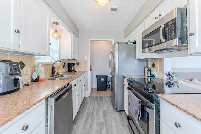 kitchen with sink, light hardwood / wood-style floors, hanging light fixtures, white cabinetry, and appliances with stainless steel finishes