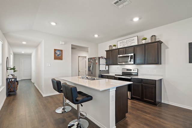 kitchen featuring a kitchen island with sink, dark hardwood / wood-style floors, a breakfast bar, appliances with stainless steel finishes, and dark brown cabinets