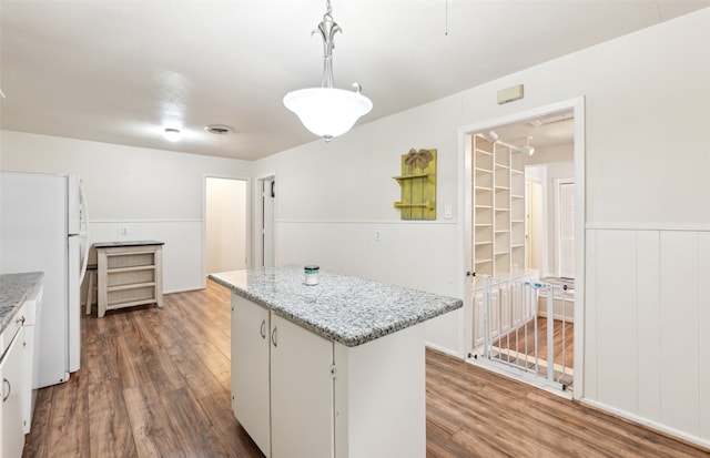 kitchen with a kitchen island, hanging light fixtures, hardwood / wood-style floors, white refrigerator, and white cabinetry