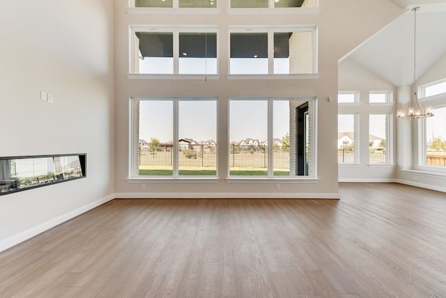 unfurnished living room with baseboards, a high ceiling, wood finished floors, and a notable chandelier