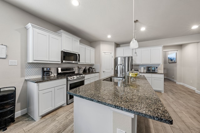 kitchen with a kitchen island with sink, stainless steel appliances, pendant lighting, decorative backsplash, and white cabinets