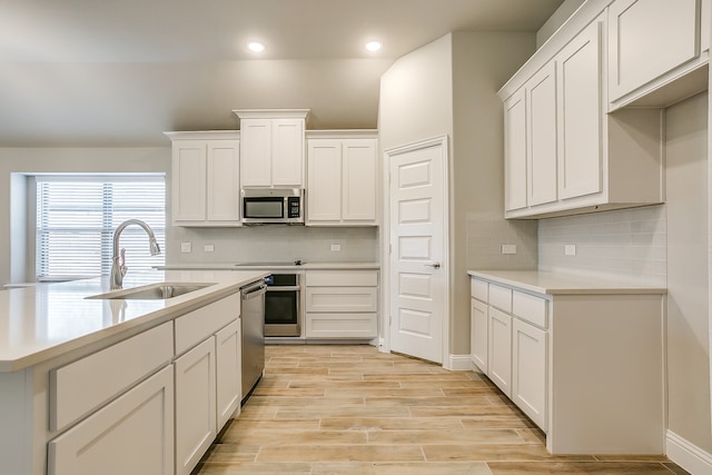 kitchen featuring white cabinets, sink, stainless steel appliances, light wood-type flooring, and decorative backsplash