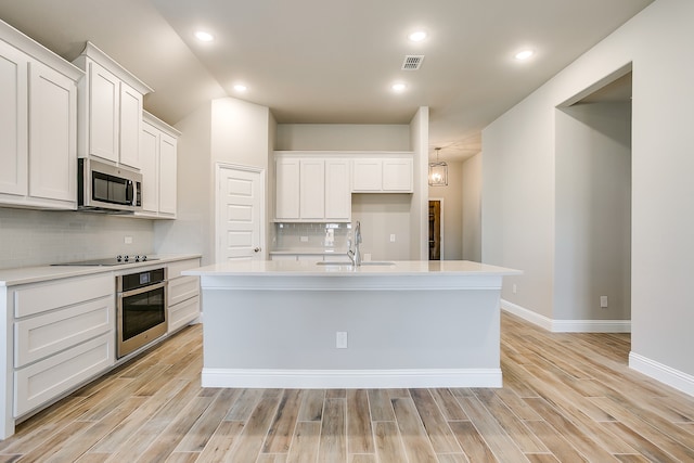 kitchen featuring tasteful backsplash, a center island with sink, sink, stainless steel appliances, and white cabinets