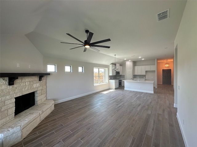 unfurnished living room with ceiling fan, vaulted ceiling, sink, a fireplace, and dark hardwood / wood-style floors