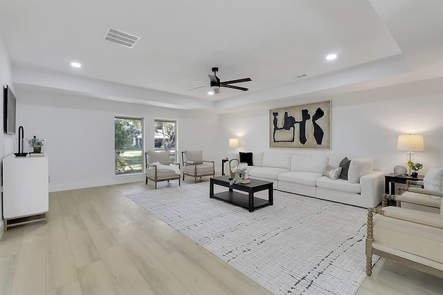 living room featuring a raised ceiling, light wood-type flooring, and ceiling fan