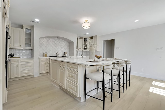 kitchen with tasteful backsplash, sink, light hardwood / wood-style flooring, a center island with sink, and a kitchen breakfast bar