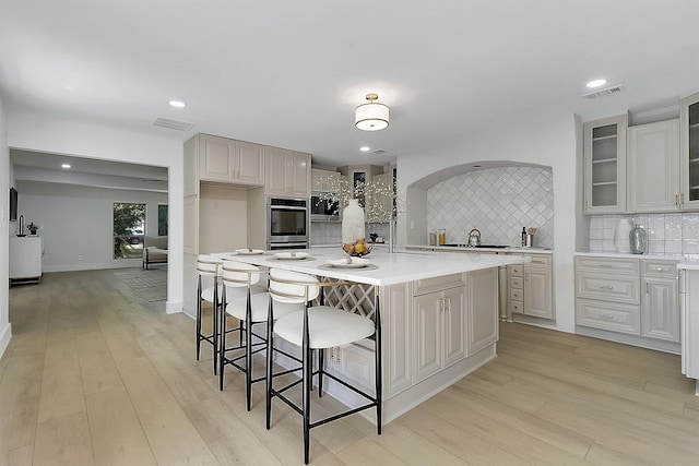 kitchen featuring light hardwood / wood-style floors, a kitchen island, a kitchen breakfast bar, stainless steel double oven, and decorative backsplash