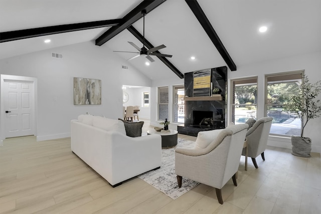 living room featuring light wood-type flooring, ceiling fan, beam ceiling, a premium fireplace, and high vaulted ceiling