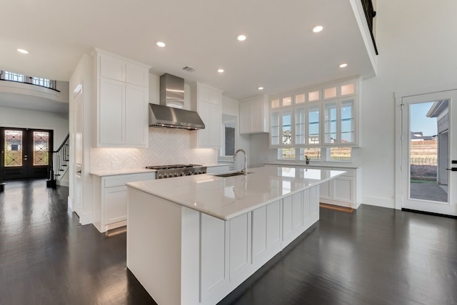 kitchen with dark wood-type flooring, a sink, white cabinetry, wall chimney range hood, and backsplash