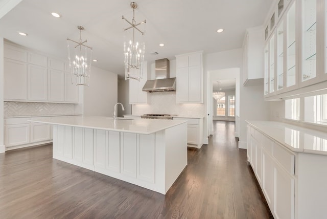 kitchen featuring dark wood-style flooring, a center island with sink, light countertops, a sink, and wall chimney range hood