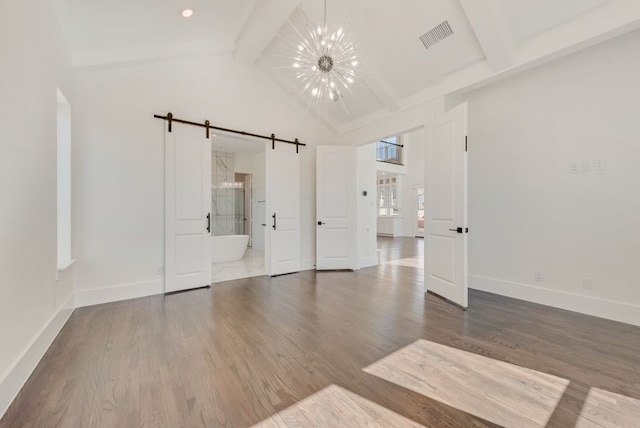 unfurnished bedroom with a barn door, wood finished floors, beam ceiling, and a notable chandelier