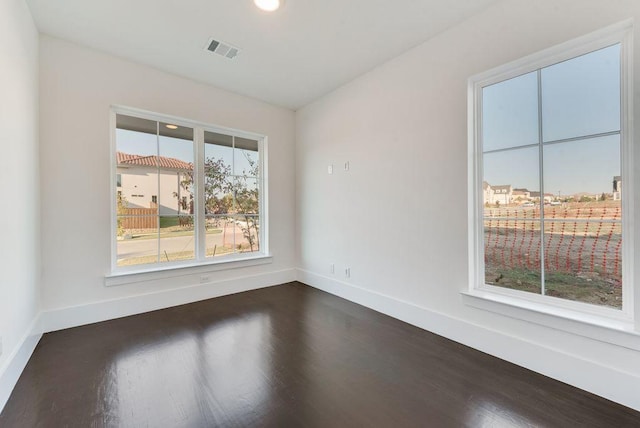 empty room with dark wood-style flooring, visible vents, and baseboards