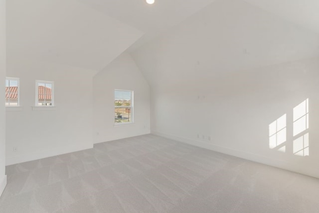 additional living space featuring light carpet, vaulted ceiling, and baseboards