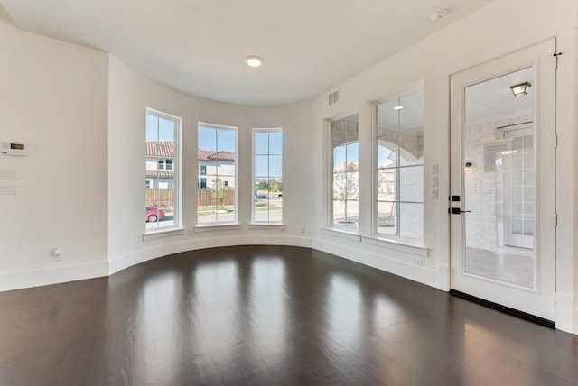 spare room with dark wood-style flooring, visible vents, and baseboards