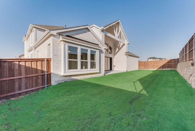 rear view of house featuring a yard, a fenced backyard, and brick siding