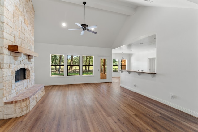 unfurnished living room with hardwood / wood-style flooring, high vaulted ceiling, ceiling fan, beamed ceiling, and a stone fireplace