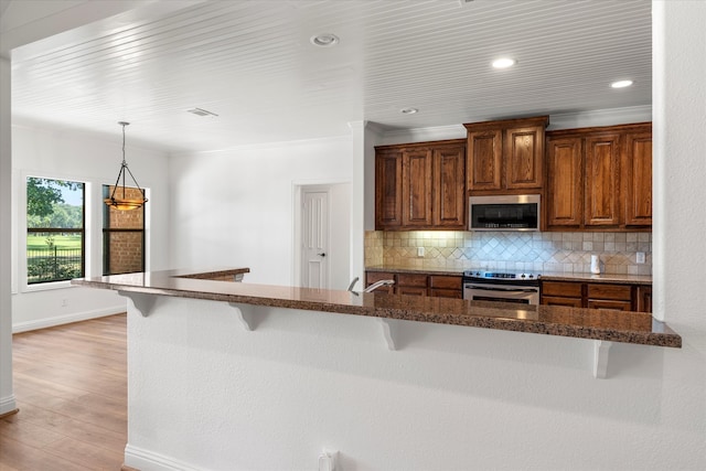 kitchen featuring light wood-type flooring, appliances with stainless steel finishes, backsplash, and a kitchen breakfast bar