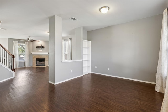 unfurnished living room featuring a tile fireplace, dark hardwood / wood-style floors, and ceiling fan