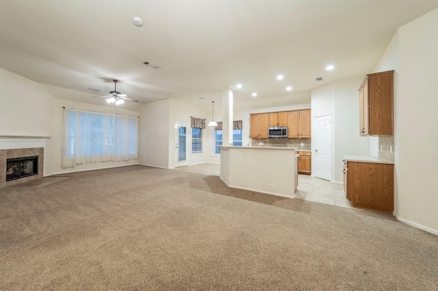 unfurnished living room featuring ceiling fan, light colored carpet, and a tiled fireplace