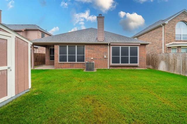 rear view of property with a shed, a yard, and central AC