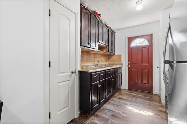 kitchen featuring stainless steel refrigerator, tasteful backsplash, dark brown cabinets, sink, and dark hardwood / wood-style floors