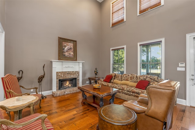 living room featuring wood-type flooring, a towering ceiling, and a brick fireplace