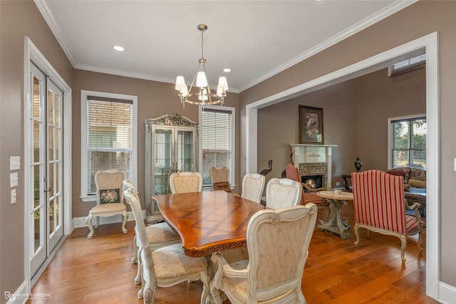 dining room featuring french doors, a brick fireplace, light hardwood / wood-style flooring, a chandelier, and ornamental molding