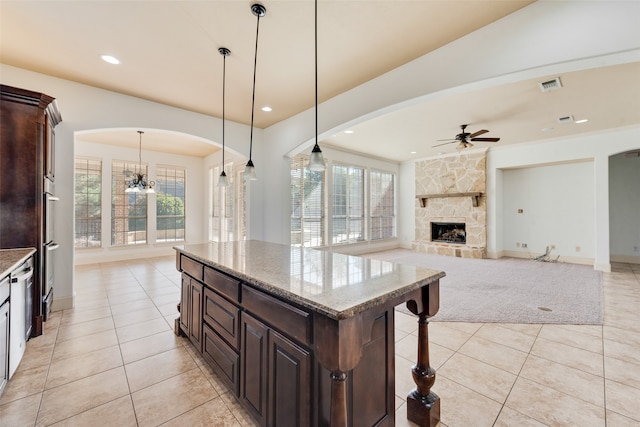 kitchen featuring decorative light fixtures, a stone fireplace, light stone countertops, a kitchen bar, and a center island