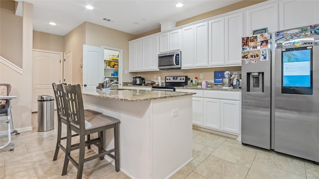 kitchen featuring an island with sink, white cabinetry, appliances with stainless steel finishes, a breakfast bar, and light stone countertops