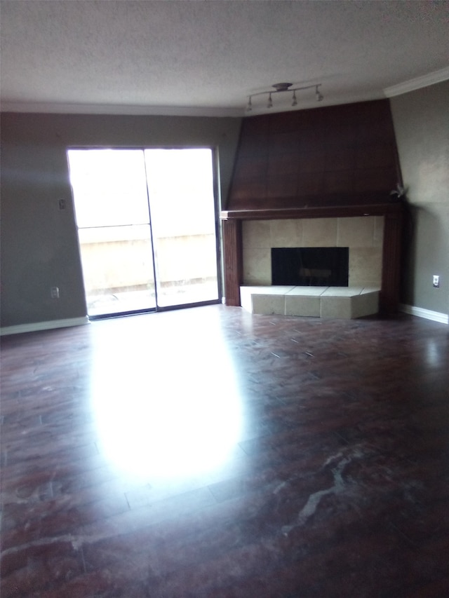 unfurnished living room featuring a fireplace, a textured ceiling, track lighting, and ornamental molding