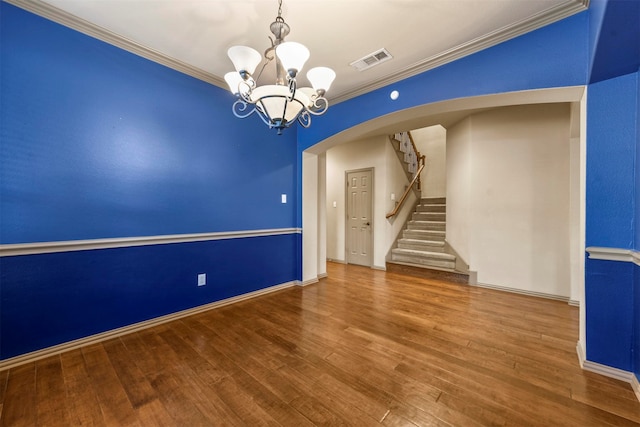 spare room featuring wood-type flooring, crown molding, and a notable chandelier