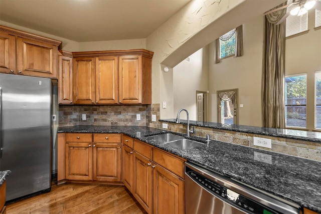 kitchen with sink, tasteful backsplash, stainless steel appliances, dark stone countertops, and light wood-type flooring