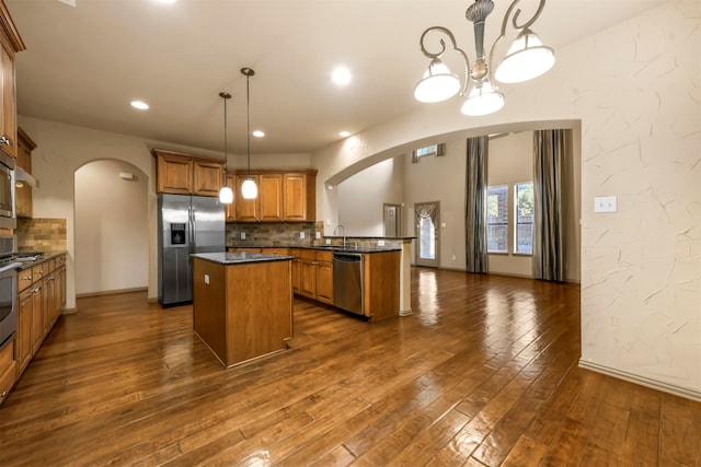 kitchen with tasteful backsplash, dark hardwood / wood-style flooring, decorative light fixtures, kitchen peninsula, and appliances with stainless steel finishes