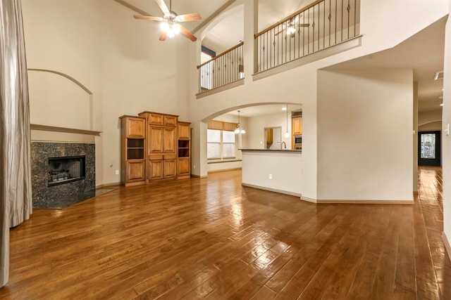 unfurnished living room with dark wood-type flooring, sink, a high ceiling, ceiling fan with notable chandelier, and a fireplace